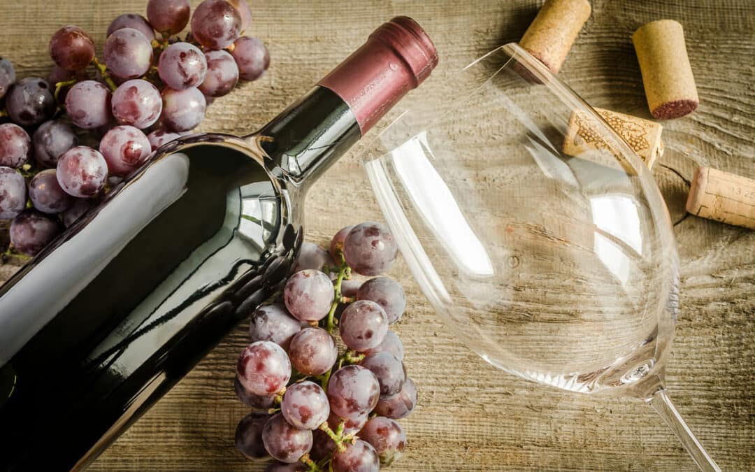 red wine bottle laying next to wine glass and red grapes