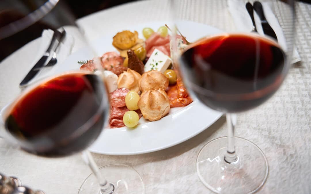 Close up of glasses with red wine and plate with snacks on white table